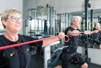 Pärchen im mittleren alter trainiert im Fitnessstudio mit einem EMS Gerät Stromimpulsgerät,...