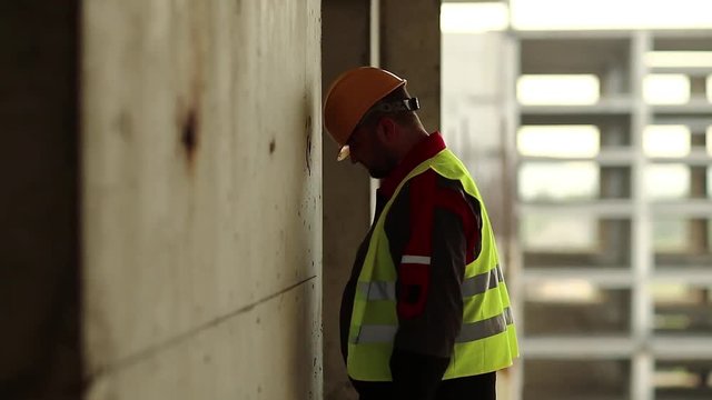 Workman knocks his head against the wall. Stressed worker in hard hat stands on construction site and knocks his head against the concrete wall, self-condemnation and self-torture