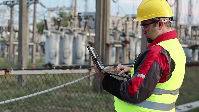 Electrician with computer on power station. Worker in hard hat at electric power plant, engineering supervision. Factory worker with tablet pc