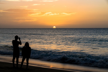 Fototapeta premium Silhouette of a couple taking photos of the sunset over the ocean
