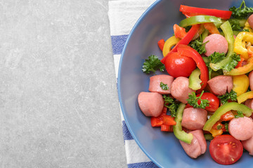 Vegetable salad with sausage in bowl on light background