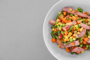 Vegetable salad with sausage in bowl on light background