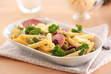 Pasta with sausage and vegetables in ceramic bowl on fabric