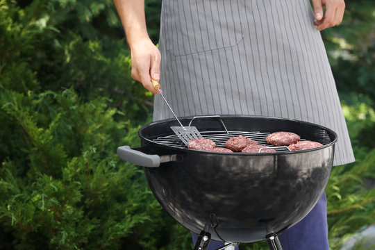 Man preparing delicious patties on barbecue grill outdoors