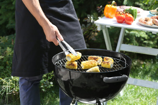 Man preparing delicious corn on barbecue grill outdoors