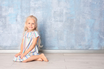 Fototapeta premium Cute little girl sitting near grey wall