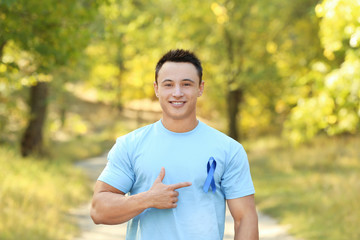 Young man pointing at blue ribbon on his t-shirt outdoors. Prostate cancer awareness concept