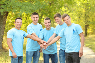 Young men in t-shirts with blue ribbons putting hands together outdoors. Prostate cancer awareness concept