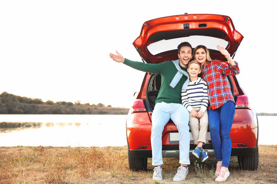 Young Family With Cute Boy Sitting In Car Trunk Near River