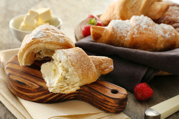Wooden board with tasty croissant on table
