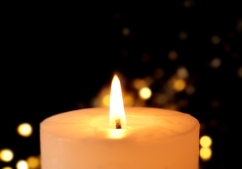 Wax candle burning on festive lights background, closeup