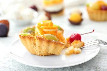 Plate with tasty fruit tartlet on table