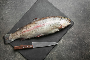 Slate plate with raw rainbow trout on grey background, top view