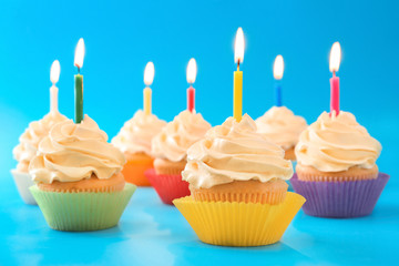 Tasty cupcakes with candles on color background