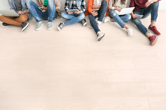 Group of teenagers with modern devices sitting on floor