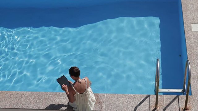 Top view of woman using her tablet on pool edge on a sunny day