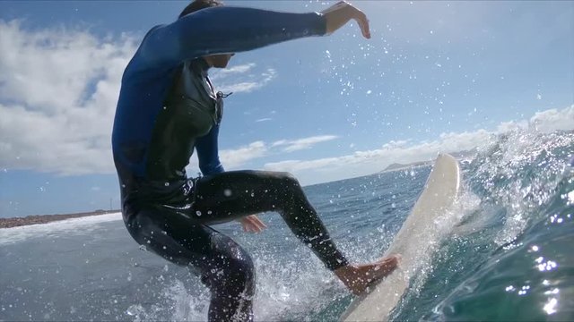 SLOW MOTION CLOSE UP: Male surfer riding blue breaking waves on a sunny day. Focused surfer carving wave and making sharp turn on his surfboard in awesome Fuerteventura. Young man having fun surfing.
