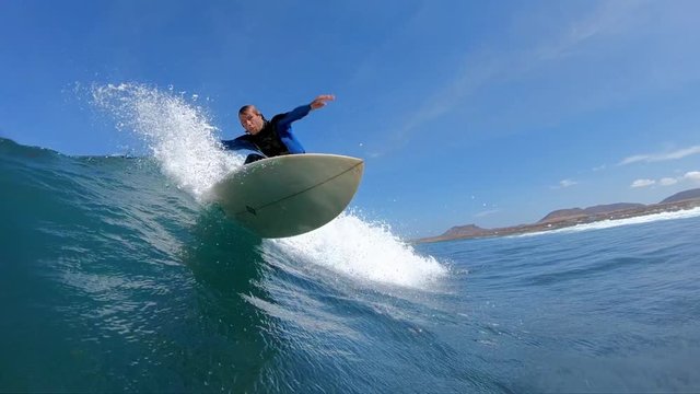 SLOW MOTION: Surfer dude making a sharp turn on his surfboard and splashes water on camera lens. Sportsman having adrenaline fun carving dangerous ocean waves. Young surfer riding epic wave in the sun