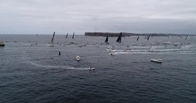 Wide panorama of Sydney Hobart Yacht race off Sydney Harbour against South head and clearance from harbour in aerial rotation with crowd of spectator boats.
