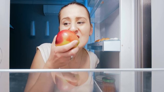 4k footage of hungry young woman sneking in fridge and biting apple