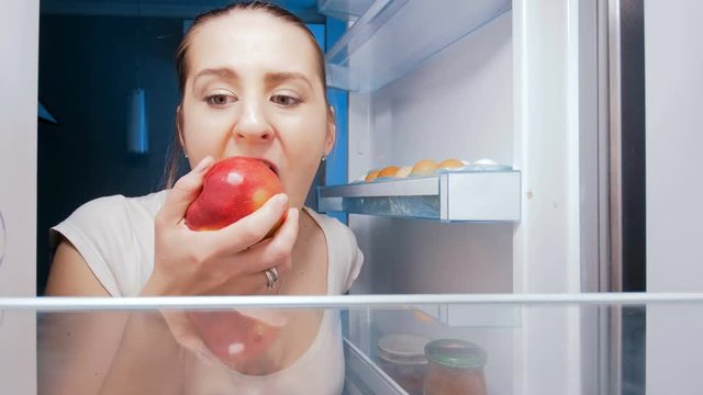 4k footage of hungry young woman sneking in fridge and biting apple. Concept of unhealthy nutrition