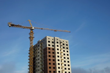 Fototapeta na wymiar A house under construction and a construction crane next to a blue sky. 