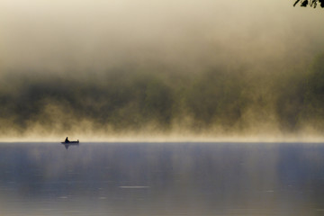 Obraz na płótnie Canvas Fisherman on a wood boat in a lake at sunrise in a foggy day