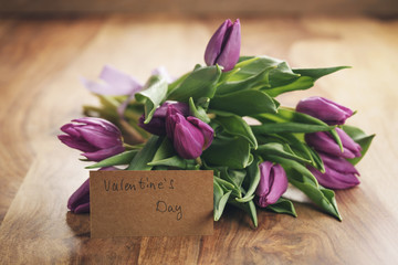 bouquet of purple tulips on wood table with paper card for valentines day