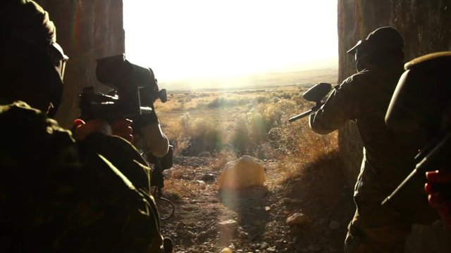 People playing paintball, running in a tunnel outside.