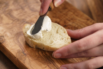 young female hands spreading cream cheese on baguette