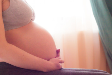 closeup of hands holding the cute belly of a pregnant woman on the ninth month. against the...