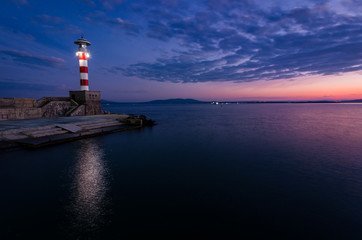 Fototapeta na wymiar colored sunset and lighting lighthouse on the sea coast