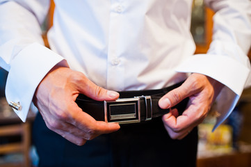 Groom fastening his black leather belt before the wedding ceremony.