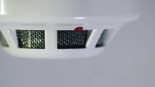 Close-up shot: The smoke detector is triggered by a trickle of dum, the red indicator lights up. White background