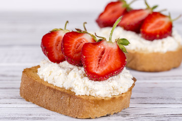Two sandwich from red strawberry, white cottage cheese and bread on the white wooden table, close up