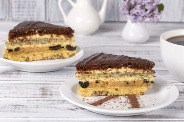 Chocolate piece of cake from biscuit dough with poppy seed, prune and walnuts and cup of coffee on the wooden table, close up
