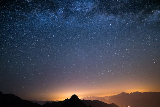 The wonderful starry sky on Christmas time and the majestic high mountain range of the Italian Alps, with glowing villages below.