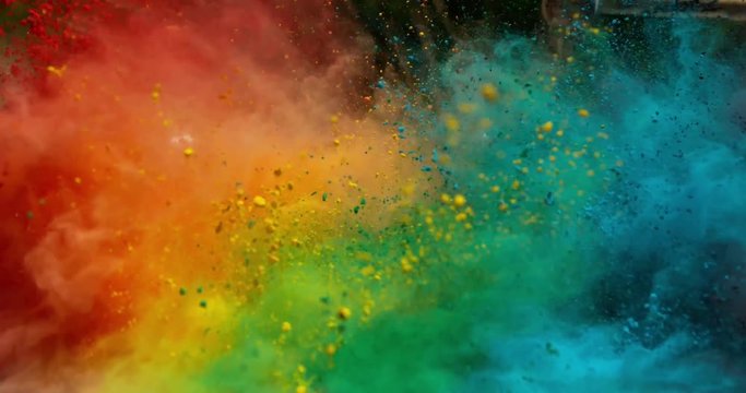 Colorful rainbow holi powder bounces off white canvas background in shockwave pattern of green blue pink and orange, slow motion, closeup