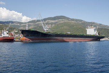 Moored tanker near the shore against the backdrop of green mountains in the summer.