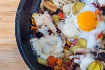 Deftiges Frühstück mit Spiegelei, Kartoffeln, Paprika, Champignons und Käse in der Pfanne