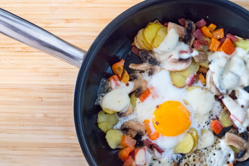 Deftiges Frühstück mit Spiegelei, Kartoffeln, Paprika, Champignons und Käse in der Pfanne
