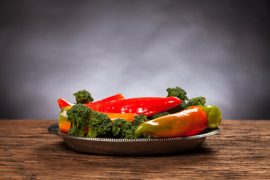 Fresh red pepperoni frigitelli and broccoli on a wooden table. Dark background. Vegan food