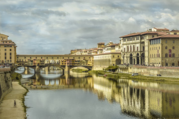 Naklejka premium florence pontevecchio bridge in a cloudy autumn morning with historical medieval palace reflecting on the river water