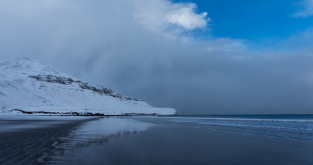 Reflection of snow-covered hill in shallow water low tide beach in Iceland in winter