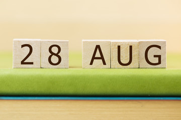 Wooden cube shape calendar for AUG 27 on green book, table.