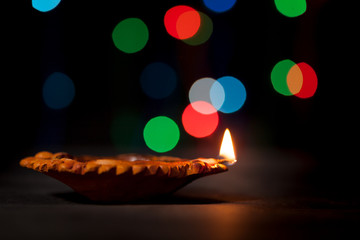 A beautiful Handmade Designer Clay Lamp with burning wick against colorful lights in the background. 