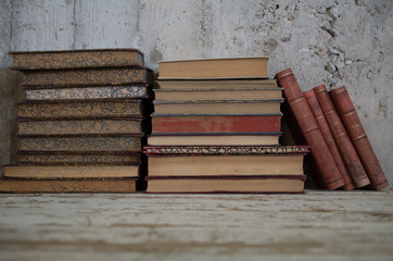 libri antichi appoggiati in verticale e orizzontali su tavolo legno e muro grezzo