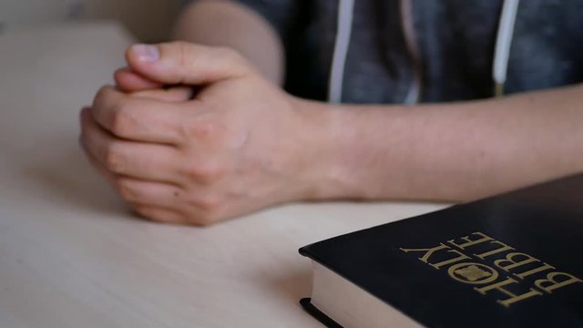 Person prays with his fingers crossed near the Holy Bible