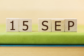 Wooden cube shape calendar for SEP 15 on green book, table.