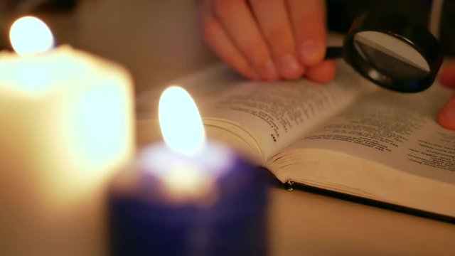 Man studying Holy Bible with blurry candles burning